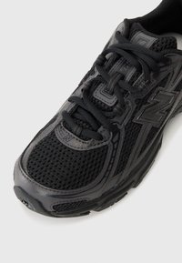 Schwarzer Sportschuh mit einem Obermaterial aus Mesh, strukturierten Overlays und gepolstertem Kragen. Enthält flache Schnürsenkel und ein Logo an der Seite.