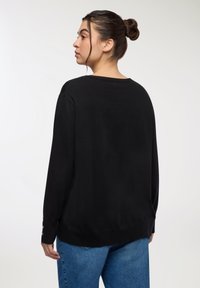 Czarny sweter z długimi rękawami i szerokim dekoltem, o gładkiej teksturze i subtelnych bocznych rozcięciach. Połączony z jasnoniebieskimi dżinsami.