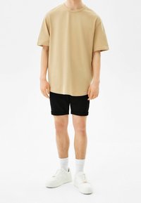 Beige puuvillane T-särk, millel on ümar kaelus, koos mustade denim-lühikeste pükstega. Jalatsiteks on valged spordijalatsid ja valged põlve sokid.