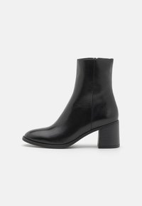 Black leather ankle boot with a rounded toe, mid-height block heel, and a smooth finish. Features a discreet side zipper.