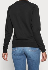 Sudadera negra con cuello redondo acanalado, mangas largas y una textura suave y lisa. Combinada con unos vaqueros de mezclilla azules.