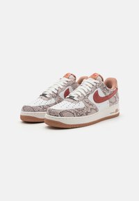White sneakers with snake-print accents in beige and grey, red Nike swoosh logo, white laces, and gum sole. Textured upper with perforations.