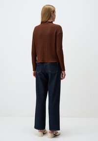 Pull en maille texturée marron avec un col montant, associé à un jean droit taille haute bleu foncé et des chaussures à talons blocs de couleur claire.