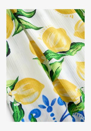 White fabric features a colorful lemon and leaf pattern in yellow and green, accented by blue floral designs. Light, textured surface visible.