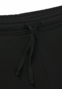 Un pantalon de survêtement noir présente une ceinture côtelée avec un lien de serrage, fabriqué dans un tissu doux et texturé, mettant en avant le confort et la fonctionnalité.