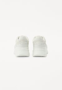 Zapatillas blancas con parte superior de cuero liso y malla, punta redondeada, suela gruesa y detalles sutiles en el talón.
