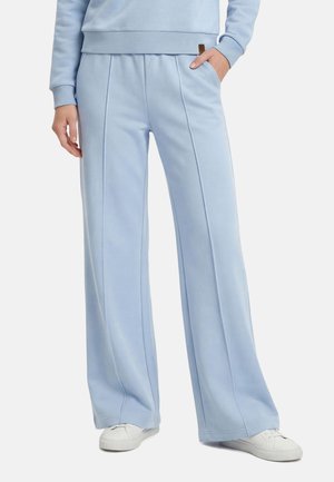 Jasnoniebieskie spodnie z szerokimi nogawkami z przednimi szwami i kieszeniami, noszone z dopasowaną bluzą i białymi trampkami.
