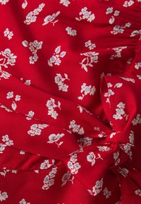 Červená látka s malými bílými a světle modrými květinovými vzory, shromážděná a se staženým uzlovým detailem.