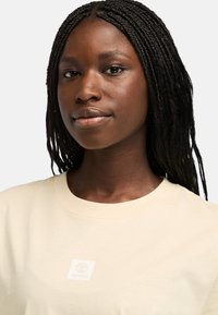 Beige bavlněné tričko s kulatým výstřihem, na hrudníku s malým logem Timberland. Hladká textura, volný střih.