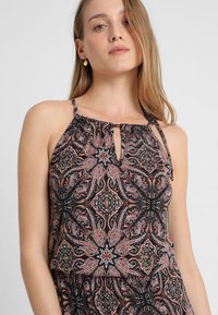 Top negro de cuello halter con intrincado patrón de paisley, con una apertura tipo ojal en el cuello y finas tiras ajustables. Textura de tela suave.