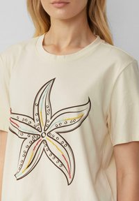 Cream-colored cotton t-shirt featuring a starfish design in black outline, decorated with colorful beads in blue, red, and yellow.