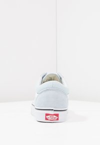 Lys blå semsket sneakers med hvite detaljer, avrundet tå og signaturrød "VANS Off the Wall" logo på hvit såle. Enkelt design.