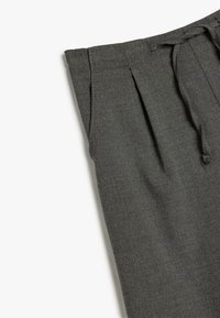 Pantalons gris texturés avec une taille à cordon et un devant plissé, présentant des lignes épurées et une silhouette ajustée.