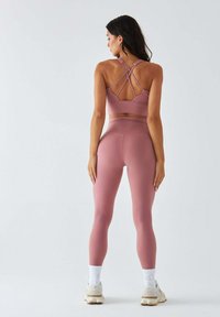 Różowy sportowy krótki top z krzyżującymi się szelkami oraz różowe legginsy z wysokim stanem, w połączeniu z białymi skarpetkami do kostek i jasnymi butami.