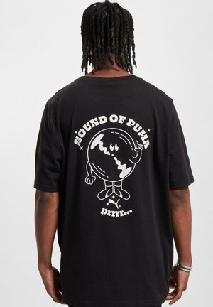 Svart t-skjorte med et grafisk illustrasjon på baksiden, med teksten "SOUND OF PUMA" og en tegneserieaktig karakter i hvitt.