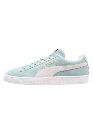 Jasnoniebieski zamszowy sneaker z białą podeszwą, białym bocznym paskiem Puma, jasnoniebieskimi sznurówkami i złotym logo "Puma Suede" z boku.