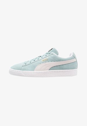 Jasnoniebieski zamszowy sneaker z białą podeszwą, białym bocznym paskiem Puma, jasnoniebieskimi sznurówkami i złotym logo "Puma Suede" z boku.