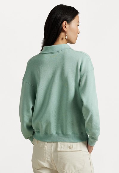 Sweatshirt verde mentă cu textură ribbed, croială casuală, guler și umeri căzuți. Asortat cu pantaloni bej deschis.