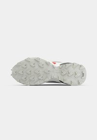 Semelle de chaussure de sport en caoutchouc gris avec des motifs de traction prononcés et une section centrale surélevée, présentant un accent rouge sur un côté.