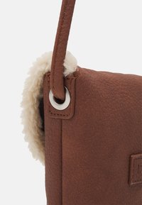 Bruine leren handtas met een textuurafwerking, voorzien van een zachte schapenvacht trim en een zilverkleurig metalen hardware detail op de schouderband.