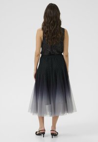 Čierny flitrový top so splývavou tylovou sukňou s ombré efektom, prechádzajúcou od tmavej po svetlú farbu, zdobenou drobnými, roztrúsenými akcentmi. Čierne sandále na opätku.