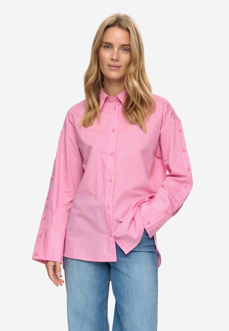 Roze gestreept overhemd met knopen, lange mouwen en grote manchetten. Voorzien van subtiele contrasterende strepen en een ontspannen pasvorm. Gecombineerd met lichtblauwe spijkerbroek.