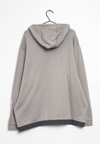 Grå hoodie med en mjuk textur, med en stor huva, långa ärmar och en kontrasterande mörk midja. Hänger på en svart krok.