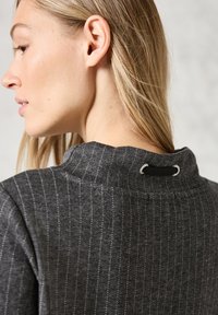 Vêtement à rayures grises avec un col haut et un détail en boucle à l'arrière. La texture semble douce, avec un éclat subtile.