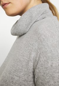 Grauer Rollkragenpullover mit geripptem Kragen, weichem Material und nahtlosem Design, das einen Teil des Halses und der Schulter einer Person zeigt.