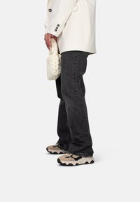 Jeans in denim nero, blazer bianco oversize, borsa bianca testurizzata e sneakers beige-neri con suole ondulate, esposti di lato.