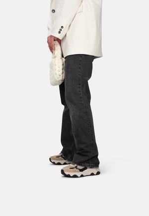 Jeans in denim nero, blazer bianco oversize, borsa bianca testurizzata e sneakers beige-neri con suole ondulate, esposti di lato.