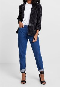 Black blazer with white polka dots, white t-shirt, blue cuffed jeans, and black high-heeled sandals; sleek, tailored design.
