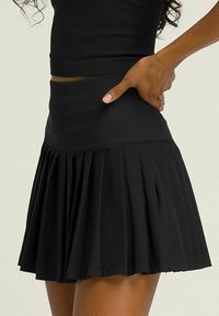 Falda plisada negra con cintura alta, hecha de un material suave y elástico. La falda llega a medio muslo y presenta un diseño acampanado.