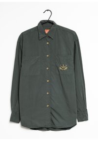 Chemise boutonnière vert foncé à manches longues, deux poches avant, boutons dorés et motif brodé sur la zone de la poche gauche.