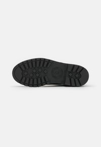Semelle de chaussure en caoutchouc noir avec un motif de semelle texturé, comportant des grips multidirectionnels et un logo circulaire au centre.