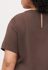 Brown short-sleeve top with a textured fabric and a keyhole opening at the back. Clean lines and simple design.