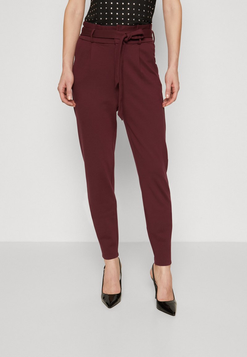 Burgundy tailored trousers with a tie waist and side pockets, featuring a tapered leg and smooth fabric, paired with black pointed-toe heels.