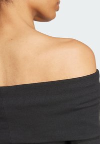 Svart rippet off-the-shoulder topp med vid utringning og tett passform som fremhever hudtonen på bare skuldre.
