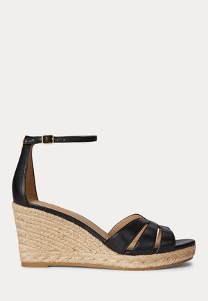 Czarna skórzana sandałka na koturnie z plecioną platformą z juty, otwartym noskiem i wyciętymi paskami oraz paskiem wokół kostki z małą złotą klamrą.