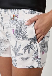 Shorts en tissu blanc avec un motif tropical dessiné à la main en noir, présentant des feuilles vertes et des accents floraux roses. Comprend des poches latérales.