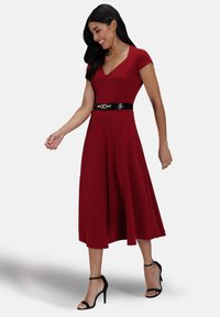 Red, knee-length dress with a V-neck and short sleeves, fitted waist, flared skirt, paired with a black belt and black sandals.
