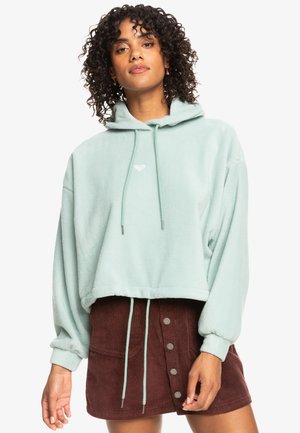 Mint green cropped hoodie in soft fleece with drawstring hood, featuring a small logo and elasticized cuffs, paired with a brown corduroy skirt.