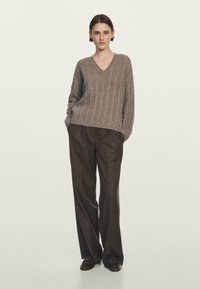 Maglione a V in maglia cable di colore marrone chiaro, abbinato a pantaloni a gamba larga e vita alta di colore marrone scuro. Tessuto morbido, vestibilità comoda.