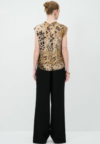 Top sin mangas color canela con estampado de leopardo, con dobladillo redondeado y detalle de botones en la espalda, combinado con pantalones de pierna ancha negros de cintura alta.
