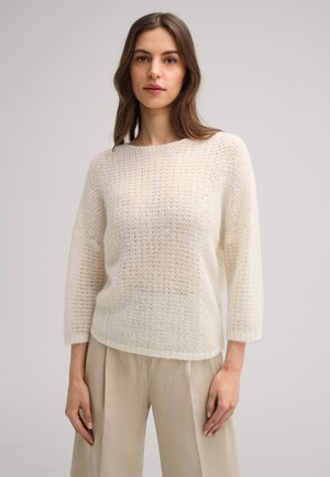 Lightweight, knitted cream sweater with a loose fit, three-quarter sleeves, and a textured pattern, paired with beige trousers.