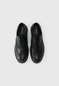 Chaussures en cuir noir à lacets présentant un design en aile, des détails en brogue et une semelle en caoutchouc pour une meilleure adhérence. Textures lisses et perforées.