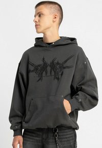 Czarny, oversize bluza z kapturem, wykonana z miękkiego materiału; posiada graficzny nadruk, kieszeń kangurka oraz napy na rękawach.