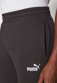 Black athletic pants made of soft fabric, featuring a ribbed waistband, side pockets, and a white Puma logo on the leg.