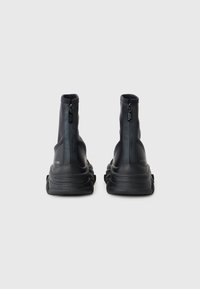 Bottines noires à fermeture éclair avec une finition lisse et mate, dotées d'une semelle épaisse et d'un logo discret à l'arrière.