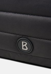 Czarna, wypchana torba z teksturowanej tkaniny, z okrągłym logo wytłoczonym z literą "B" oraz kontrastowym przeszyciem wzdłuż szwów.